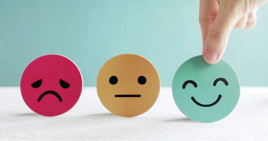 Graphic showing three round faces representing emotions. From left to right: a pink sad face with a frown, an orange neutral face, and a green happy face being picked up by a hand.