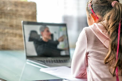 An image of the back of a student who watches a teacher on a laptop screen.