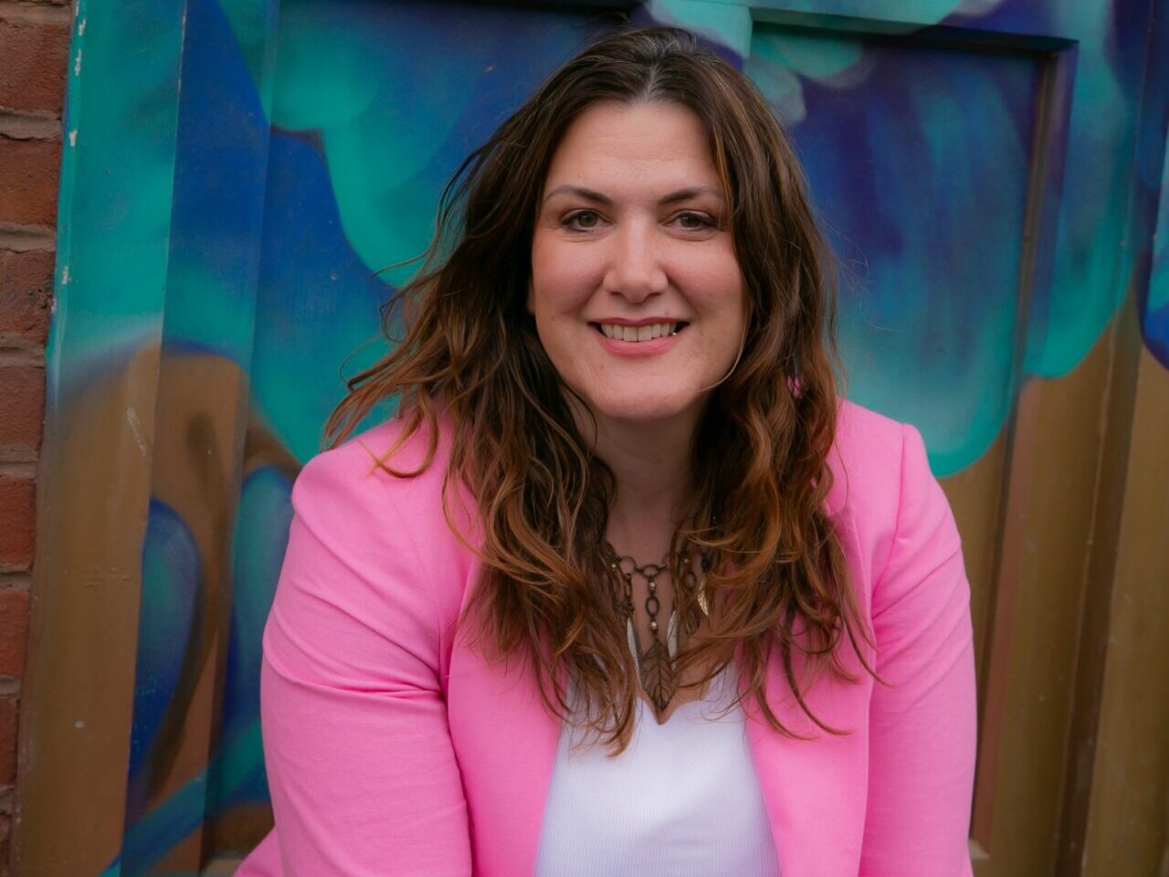 An image of Isabelle Pearcey. She is smiling, has long auburn hair, and Is wearing a pink suit jacket and white top.