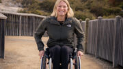 Paralympic athlete Sammi Kinghorn in her wheelchair outdoors on a scenic pathway surrounded by nature