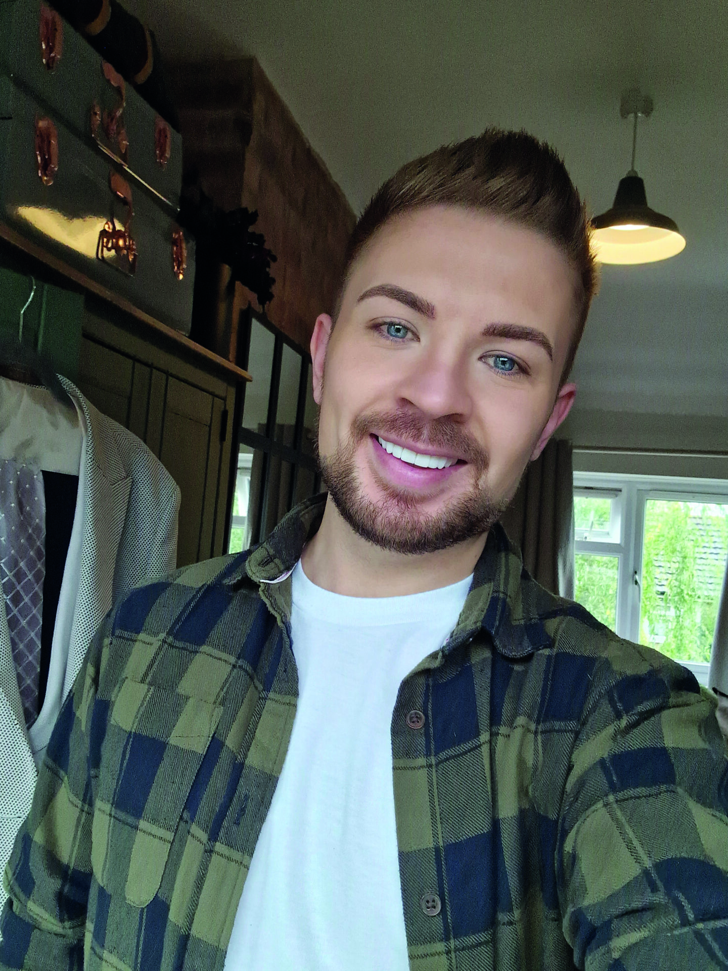 An image of Luke Manton. He is smiling, has short brown hair and a circle beard, and is wearing a dark green and black chequered flannel and a white t-shirt.