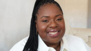 An image of Helen Ewumi. She is smiling, has long black braided hair and is wearing a white shirt.