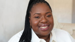 An image of Helen Ewumi. She is smiling, has long black braided hair and is wearing a white shirt.