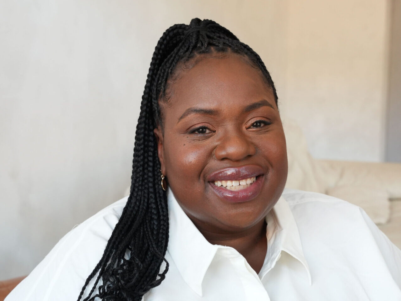 An image of Helen Ewumi. She is smiling, has long black braided hair and is wearing a white shirt.