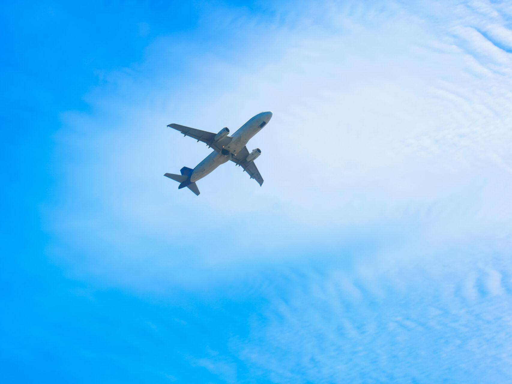 An airplane seen from below with a bright blue sky behind.