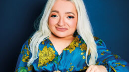An image of Samantha Renke. She is smiling, has long blond hair and is wearing a blue and yellow floral dress. She is using a wheelchair.