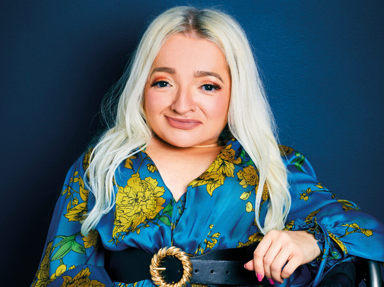 An image of Samantha Renke. She is smiling, has long blond hair and is wearing a blue and yellow floral dress. She is using a wheelchair.