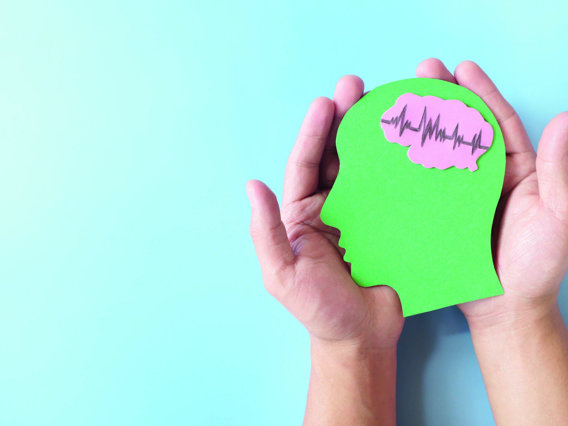 A stock image of hands holding a green human head profile cutout with a healthy brain, set against a blue background.