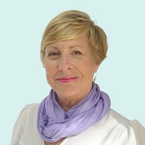 An image of Jane Hatton. She is smiling, has short swept blond hair and is wearing a silk purple scarf and a white blouse.