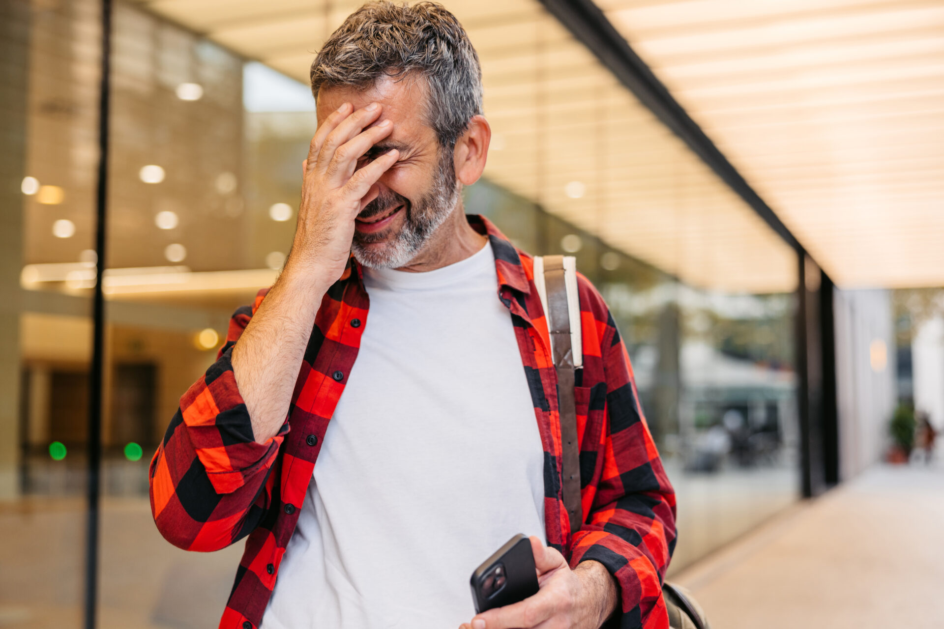A stock image of a mature man holding his hand to his face remembering something while using his smart phone on the street.