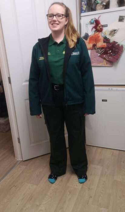 An image of Lucy Gatward. She is smiling, is wearing glasses and a dark green student paramedic uniform and black University of Surrey hoodie.