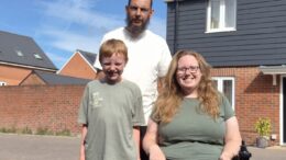 An image of Lucy Gatward and her partner and son outside a house on a sunny day. Lucy is using a wheelchair and wearing a green t-shirt and black leggings.