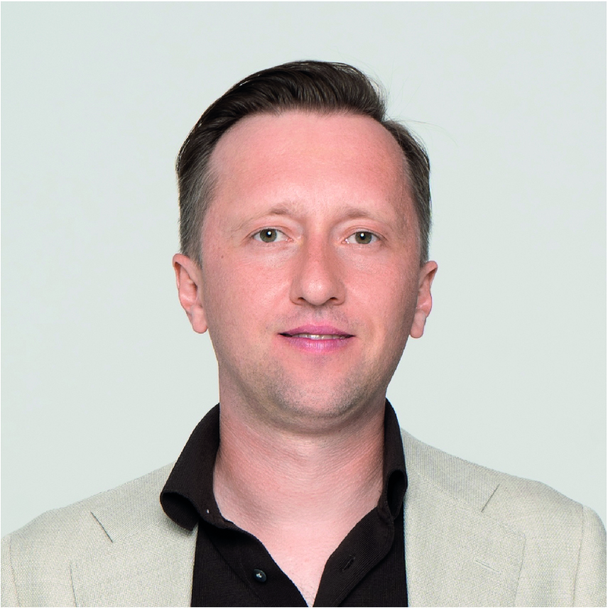 An headshot of Mykhailo Kalitkin. He is smiling, has short brown hair and is wearing a cream suit jacket and black shirt.