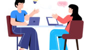 A cartoon graphic of a man and a woman discussing ideas while they work on laptops at a table. There is a lightbulb and a speech bubble element above their heads, representing ideas of discussion and understanding.